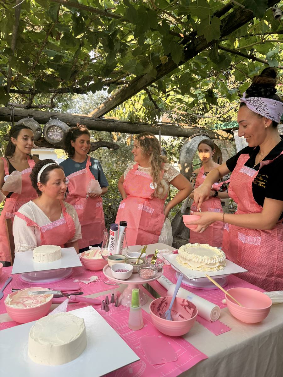 La pasticcera mostra la torta decorata al gruppo sotto il pergolato
